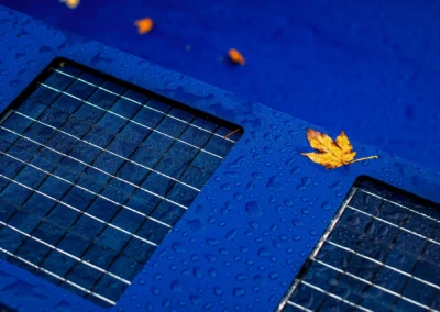 Kék felületű napkollektor vízcseppekkel és egy sárga falevéllel díszítve.