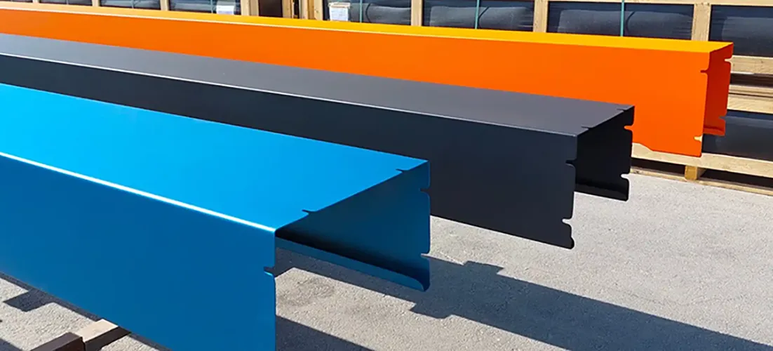 Trois profilés métalliques de couleurs bleu, noir et orange sont alignés horizontalement sur un sol en béton.