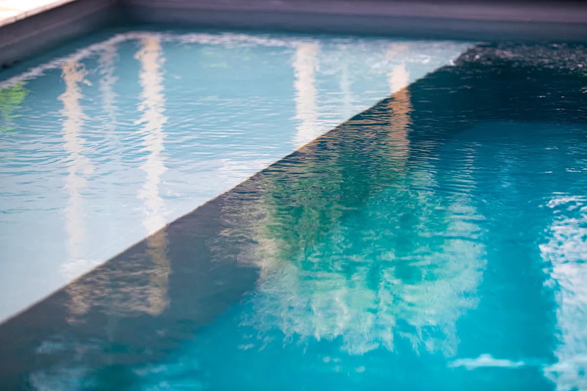 Surface d'une piscine avec de l'eau claire et des reflets de structures environnantes visibles.