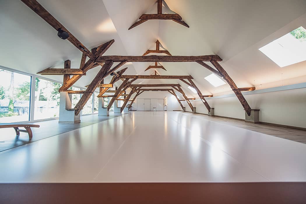 Plafond avec poutres en bois apparentes dans une grande pièce lumineuse avec piscine intérieure couverte et fenêtres panoramiques.