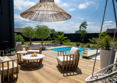 Kerti terasz medencével, fa bútorokkal és napernyővel, körülötte zöld növények és fák.