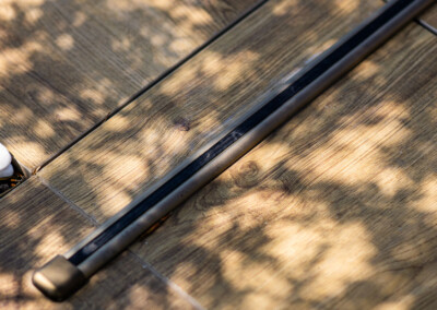 Fa fapadlón árnyékokkal borított fémrúd látható, mellette fehér kavicsok.