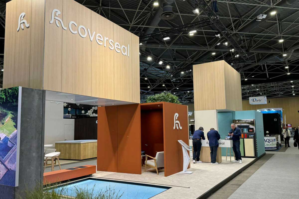 Stand d'exposition Coverseal avec structures en bois clair et panneaux orange, deux personnes interagissent près d'un comptoir.
