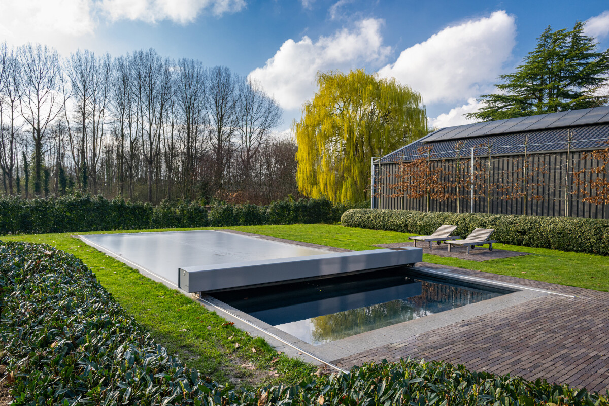 Gros plan sur l'habillage de la Coverseal grise au bord de la piscine, avec en arrière-plan les transats et la maison en pierre.